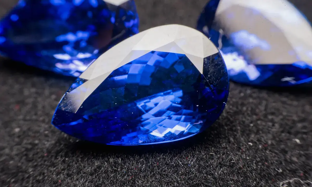 Trzy kropliste kamienie szlachetne o intensywnym, głębokim szafir kolorze, odbijające światło.