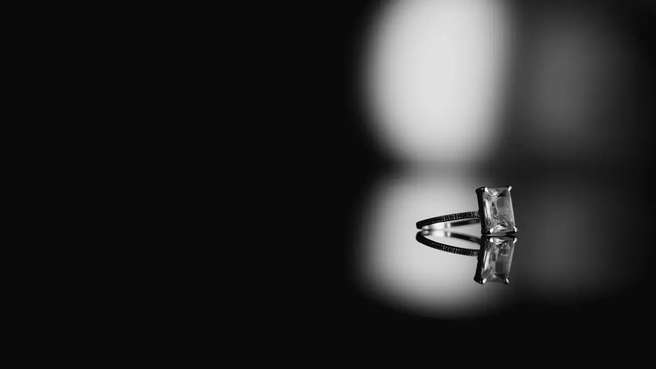 Elegancki pierścionek z prostokątnym kamieniem, który może być diamentem. Jak rozpoznać diament? Blask i odbicie sugerują jego wyjątkowość.