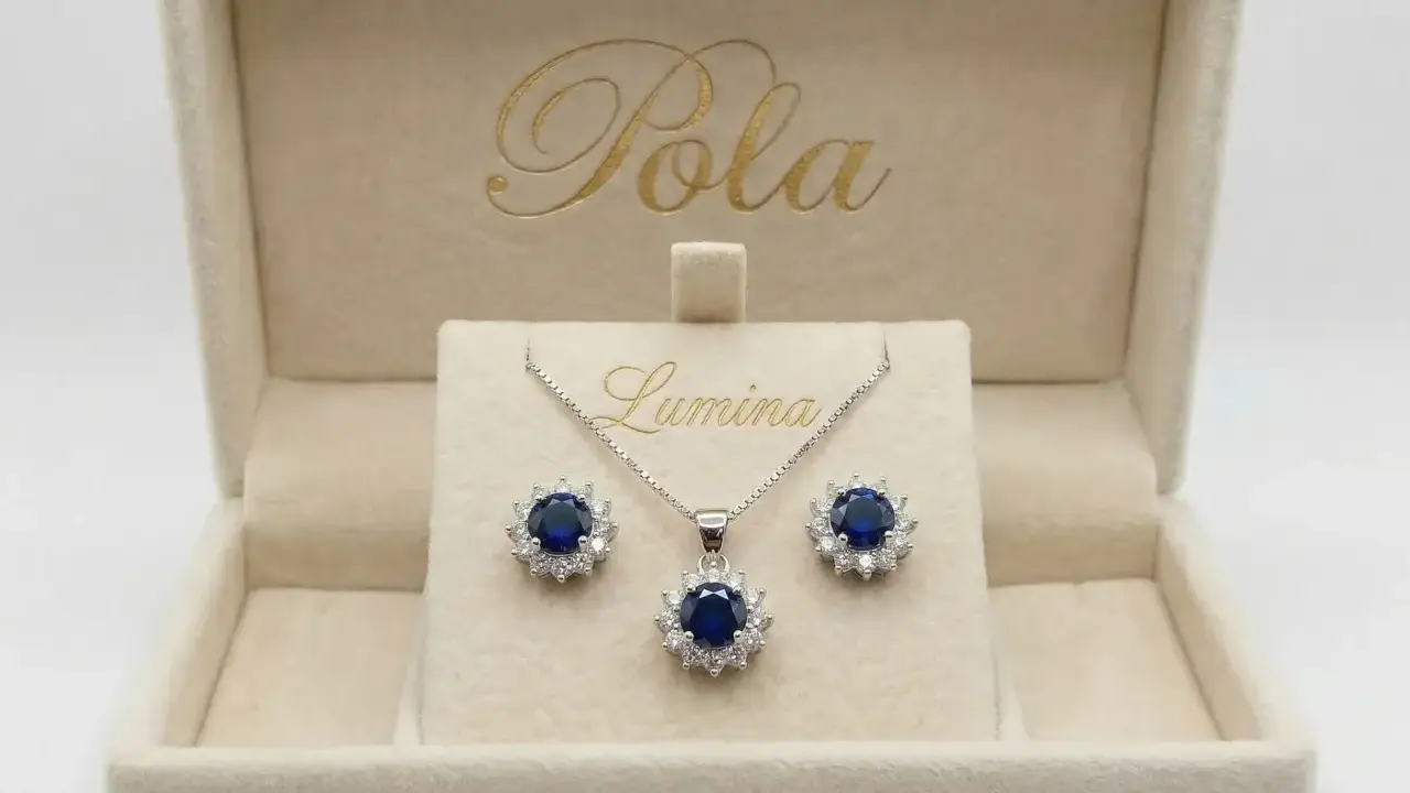 Elegancki komplet biżuterii z centralnym, głębokim szafir kamień otoczonym błyszczącymi cyrkoniami. Naszyjnik i kolczyki w pudełku z logo "Pola Lumina".