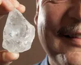 Mężczyzna z wąsami trzyma w palcach surowy, błyszczący kamień, który może być największym diamentem na świecie.