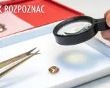 Dłoń z lupą bada mały kamień, obok pęseta. Jak odróżnić cyrkonię od diamentu?