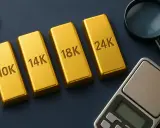 Sztabki złota o próbach 10K, 14K, 18K i 24K leżą obok siebie. Obok znajduje się lupa i waga jubilerska.