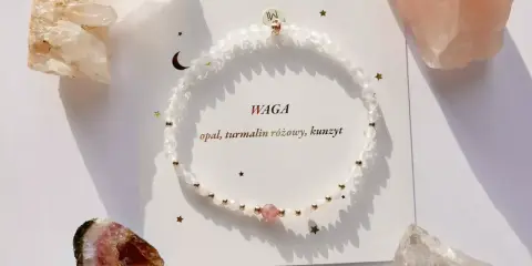 Delikatna bransoletka z białych kamieni i różowego turmalinu, otoczona surowymi klejnotami.