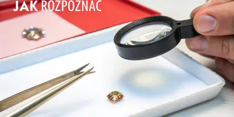 Dłoń z lupą bada mały kamień, obok pęseta. Jak odróżnić cyrkonię od diamentu?