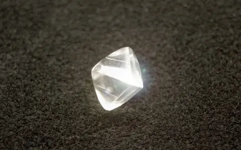 Surowy diament przed szlifowaniem, błyszczący na czarnym tle.