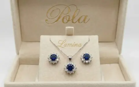 Elegancki komplet biżuterii z centralnym, głębokim szafir kamień otoczonym błyszczącymi cyrkoniami. Naszyjnik i kolczyki w pudełku z logo "Pola Lumina".