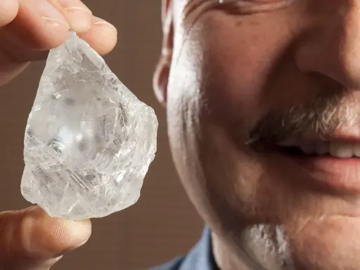 Mężczyzna z wąsami trzyma w palcach surowy, błyszczący kamień, który może być największym diamentem na świecie.
