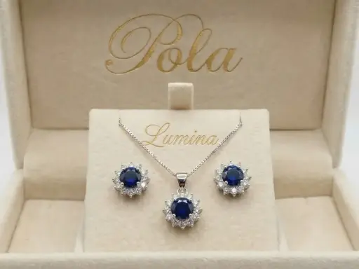 Elegancki komplet biżuterii z centralnym, głębokim szafir kamień otoczonym błyszczącymi cyrkoniami. Naszyjnik i kolczyki w pudełku z logo "Pola Lumina".