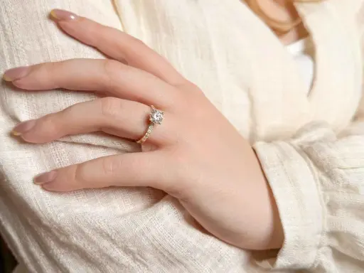 Dłoń z pierścionkiem zaręczynowym z brylantem, który wygląda na 5 karatów. Delikatny blask kamienia podkreśla elegancję biżuterii.