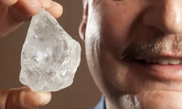 Mężczyzna z wąsami trzyma w palcach surowy, błyszczący kamień, który może być największym diamentem na świecie.