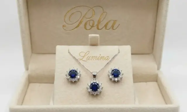 Elegancki komplet biżuterii z centralnym, głębokim szafir kamień otoczonym błyszczącymi cyrkoniami. Naszyjnik i kolczyki w pudełku z logo "Pola Lumina".